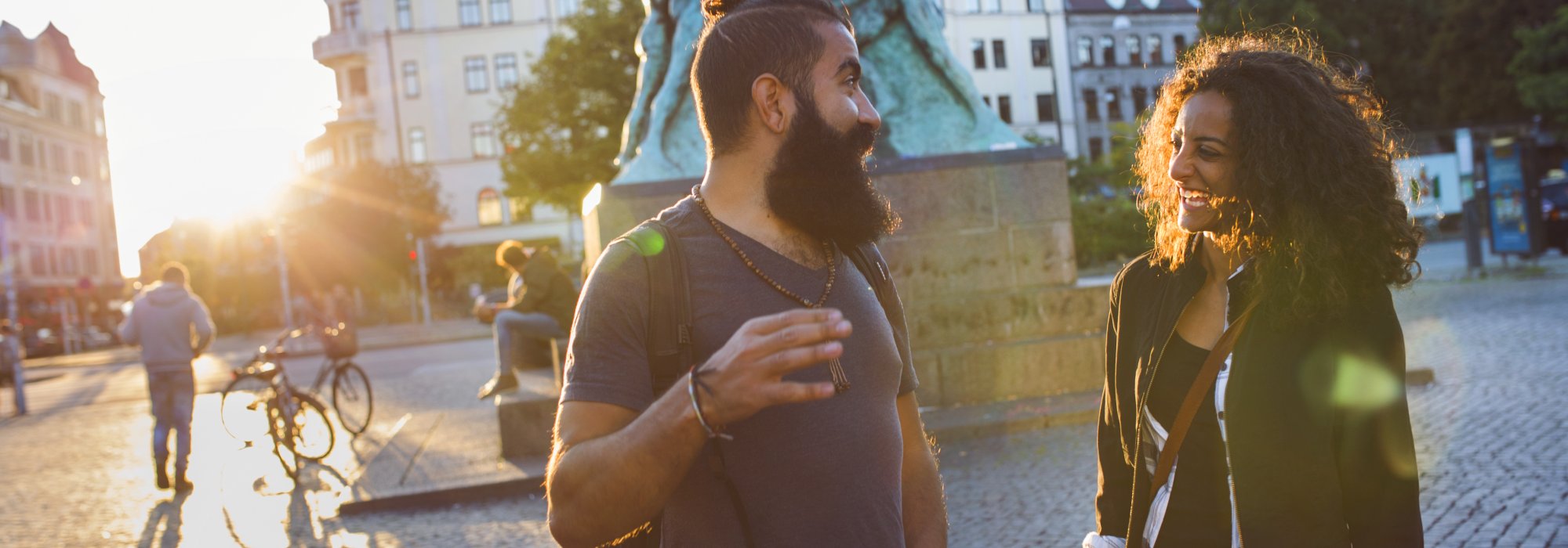 Ett par står mitt på ett torg och har ett samtal. Solen skiner och de är glada. Foto.