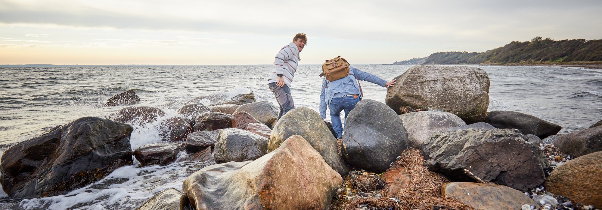 Två personer klättrar på stenar vid havet. Foto.